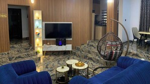 A modern living room with a flat-screen TV, blue sofas, a hanging chair, and a marble floor. - Size99 Apartment and Suites (Owerri)
