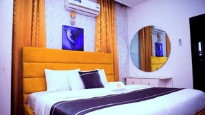 A hotel room with a large bed, a bedside table, a mirror, and an air conditioning unit. - Size99 Apartment and Suites (Owerri)