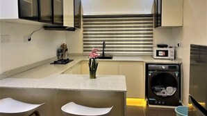 A compact kitchen with a built-in microwave, a coffee machine, and a washing machine. - Size99 Apartment and Suites (Owerri)