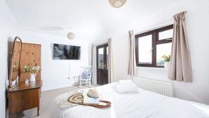 A bedroom with a bed, a wooden dresser, a television, a window with curtains, and a radiator. - Wheal Frances -Hot Tub - Free Parking - Free Wi-Fi - Accessible (Helston)