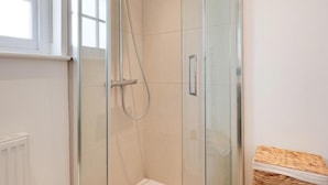 A glass-enclosed shower with a white tiled wall, a visible shower control panel, and a wicker basket on a shelf. - House in Central London - Sleeps up to 16 (London)