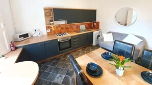A compact kitchen with dark cabinets, a microwave, a stove, and a washing machine. - House in Central London - Sleeps up to 16 (London)