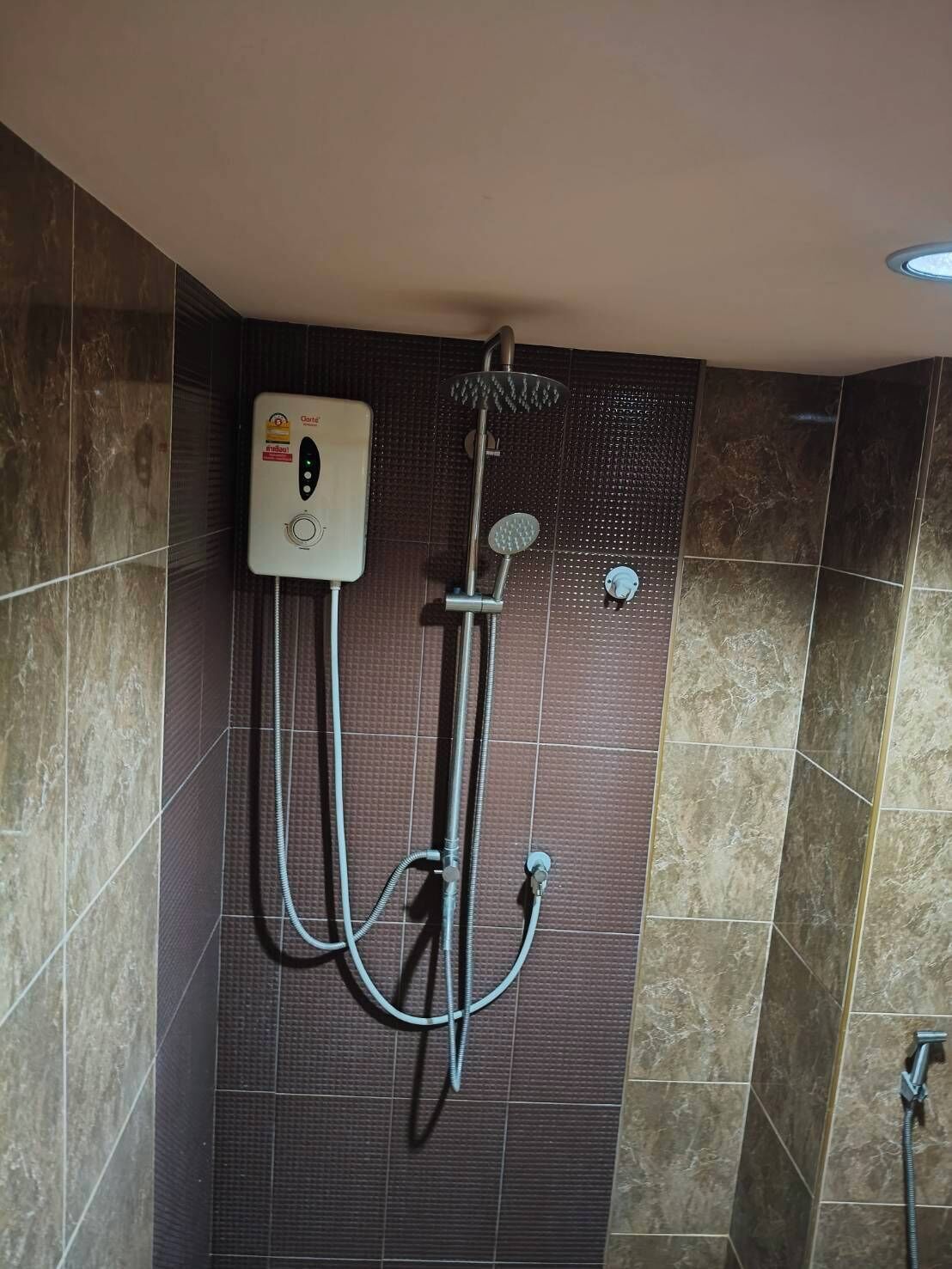 A shower with a control panel, a handheld showerhead, and a wall-mounted faucet.