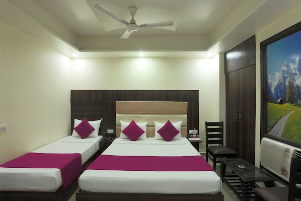 A hotel room with two beds, a desk, a chair, a TV, and a ceiling fan.