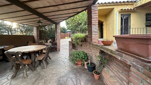 An outdoor patio with a wooden table and chairs, surrounded by potted plants and a brick wall. - Ideal Holiday Rental House for Families Near the Beach (Calonge)