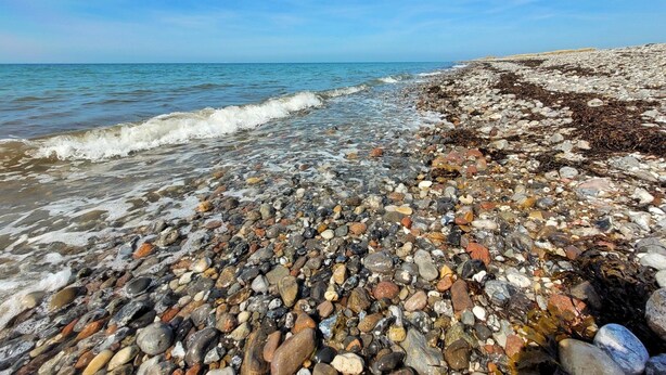 En stenstrand med klart vatten och en klar himmel.