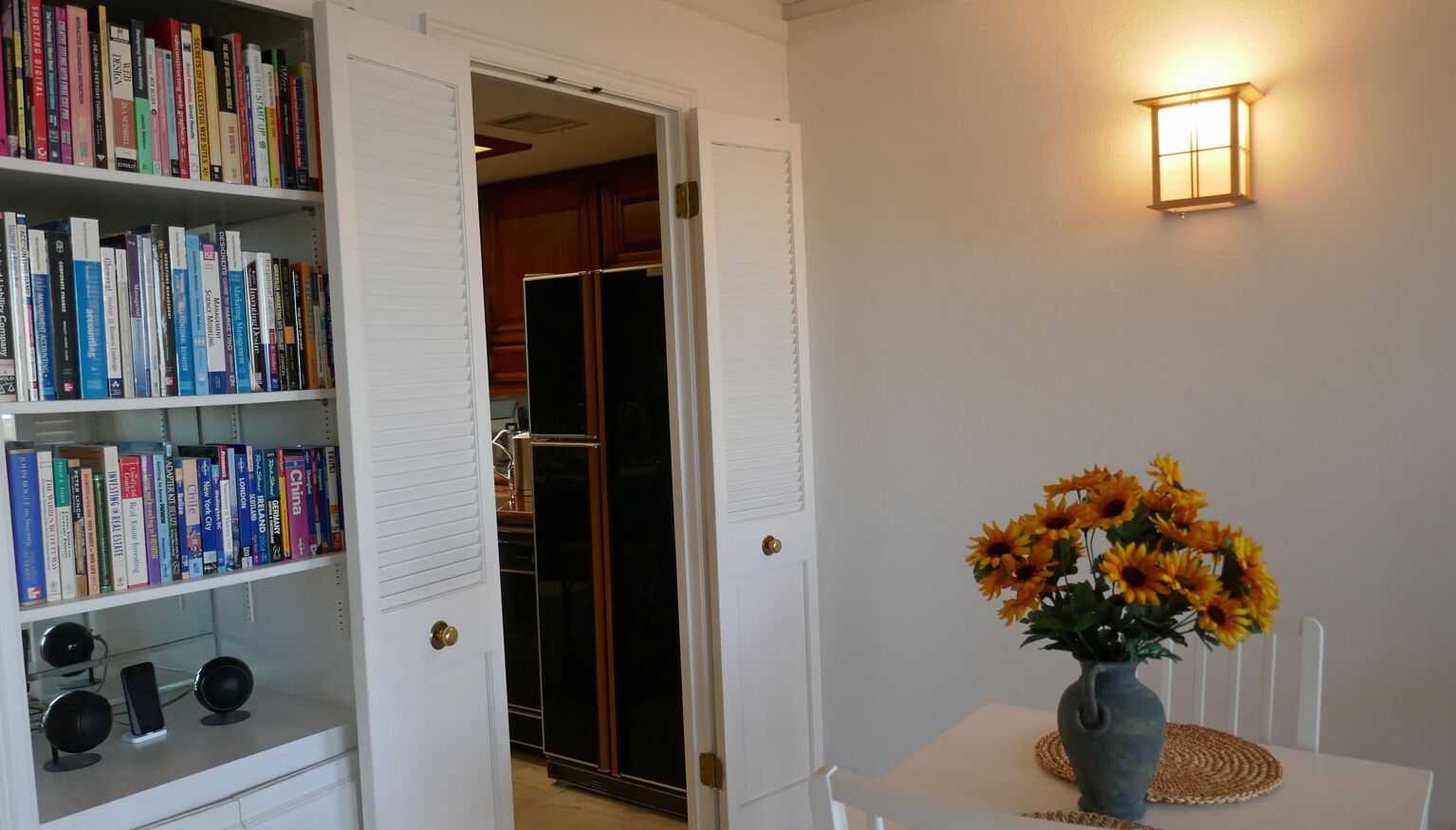 Ein Zimmer mit Bücherregal, einer Blumenvase und einer Wandleuchte.