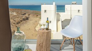Un balcon offrant une vue dégagée sur la mer, une bouteille de vin, un bol d’olives et une chaise blanche.