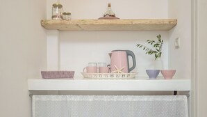 Un coin cuisine avec un plan de travail blanc, une étagère en bois au-dessus et un rideau blanc en dessous.