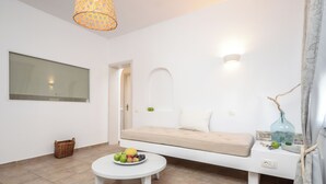 Un salon moderne avec un canapé, une table ronde sur laquelle sont disposés des fruits, un panier en osier et un luminaire fixé au mur.