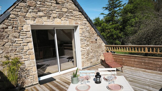 A stone building with a wooden deck, a table set for dining, and a bench. - Guergonet, Cosy 2-bedroom accomodation (Châtelaudren-Plouagat)