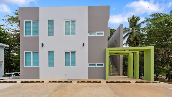 A modern building with a grey facade, multiple windows, and a green entrance.