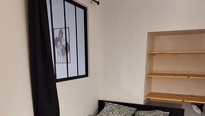 Ein Schlafzimmer mit einem Bett, einem Fenster mit Vorhang und einer Holzkonsolenwand.