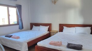 A hotel room with two wooden beds, a small round table, an air conditioning unit, and a wall-mounted light fixture.
