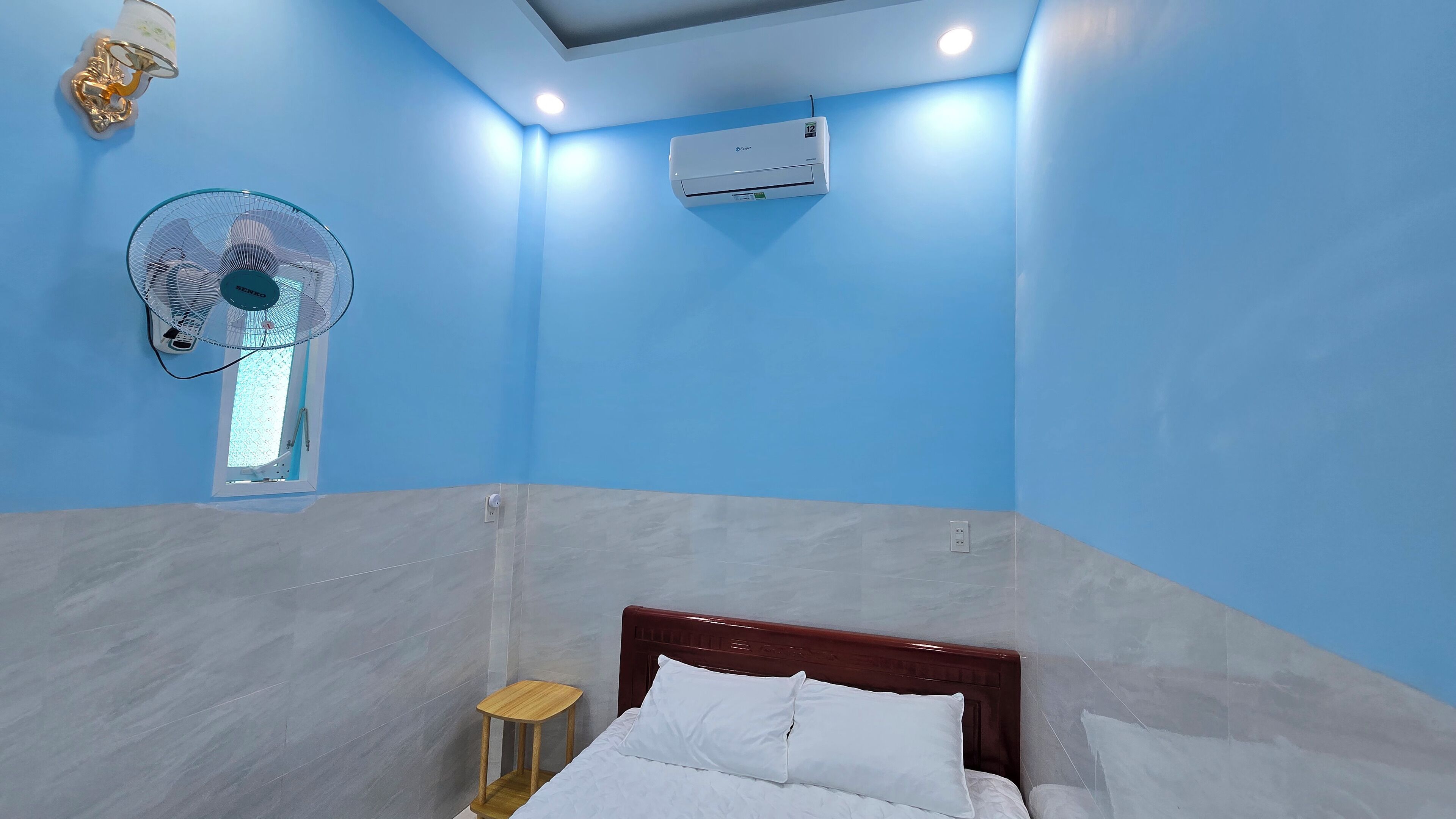 Ein Schlafzimmer mit Bett, Wandklimaanlage, Deckenventilator und kleinem Fenster.