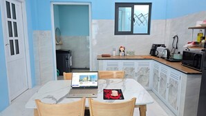 A modern kitchen with a dining area, featuring a laptop on the table, a microwave, and various kitchen appliances.