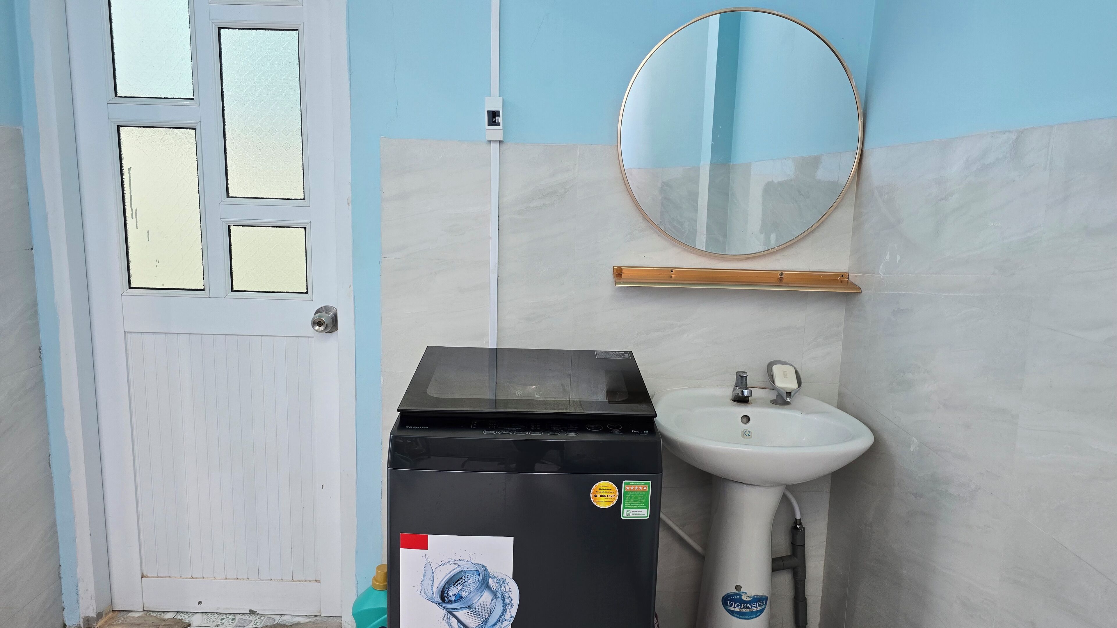 Une salle de bain avec un lavabo blanc, un miroir et un appareil électroménager noir.