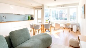 A modern living room with a sofa, a dining area with chairs, and a kitchen with cabinets. - Apartment With a View of the Marina (Ostend)
