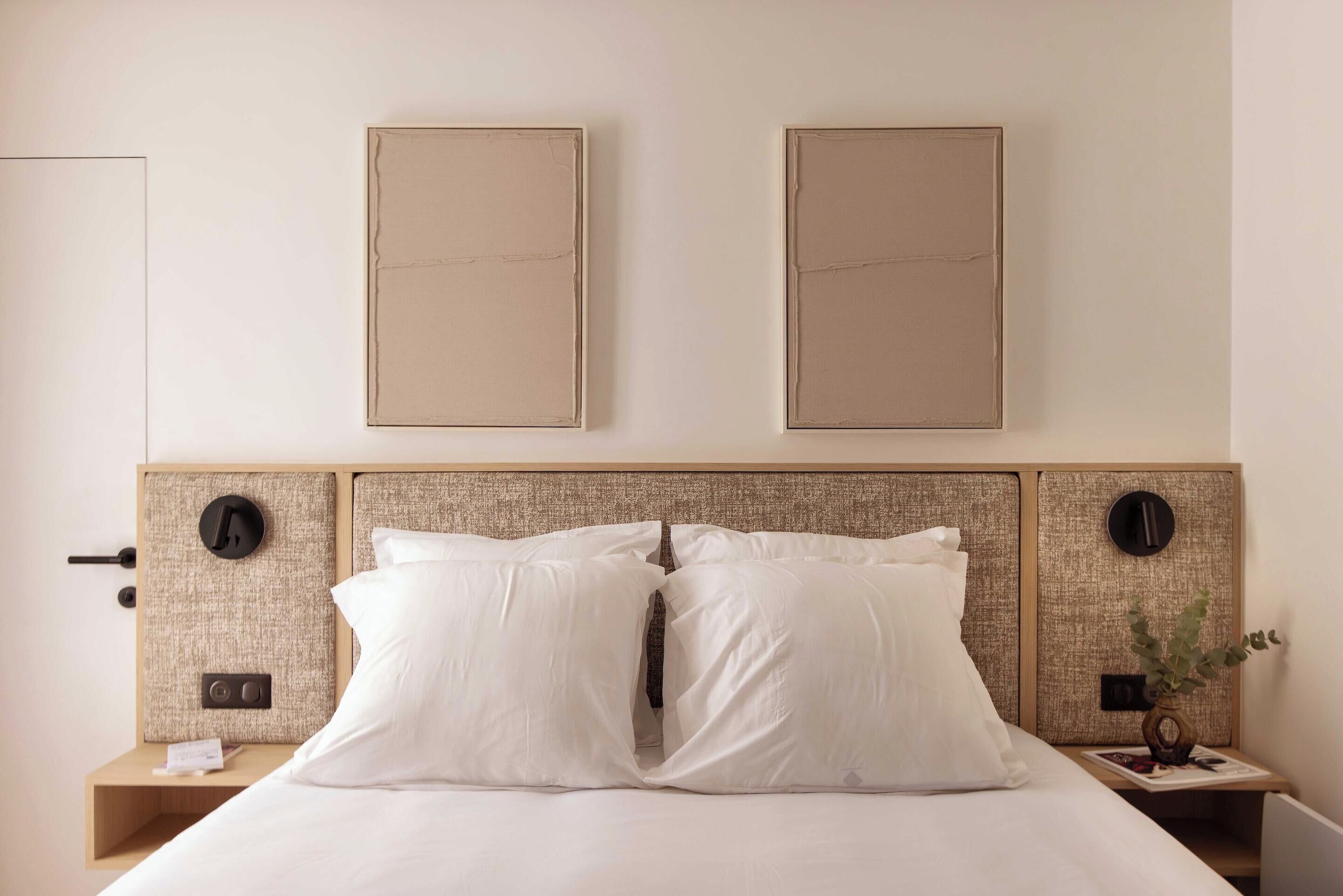A hotel room with a bed, two bedside tables, a headboard, and two framed pictures on the wall.