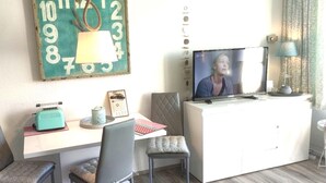Un salon avec une télévision, une horloge, une petite table et une chaise.