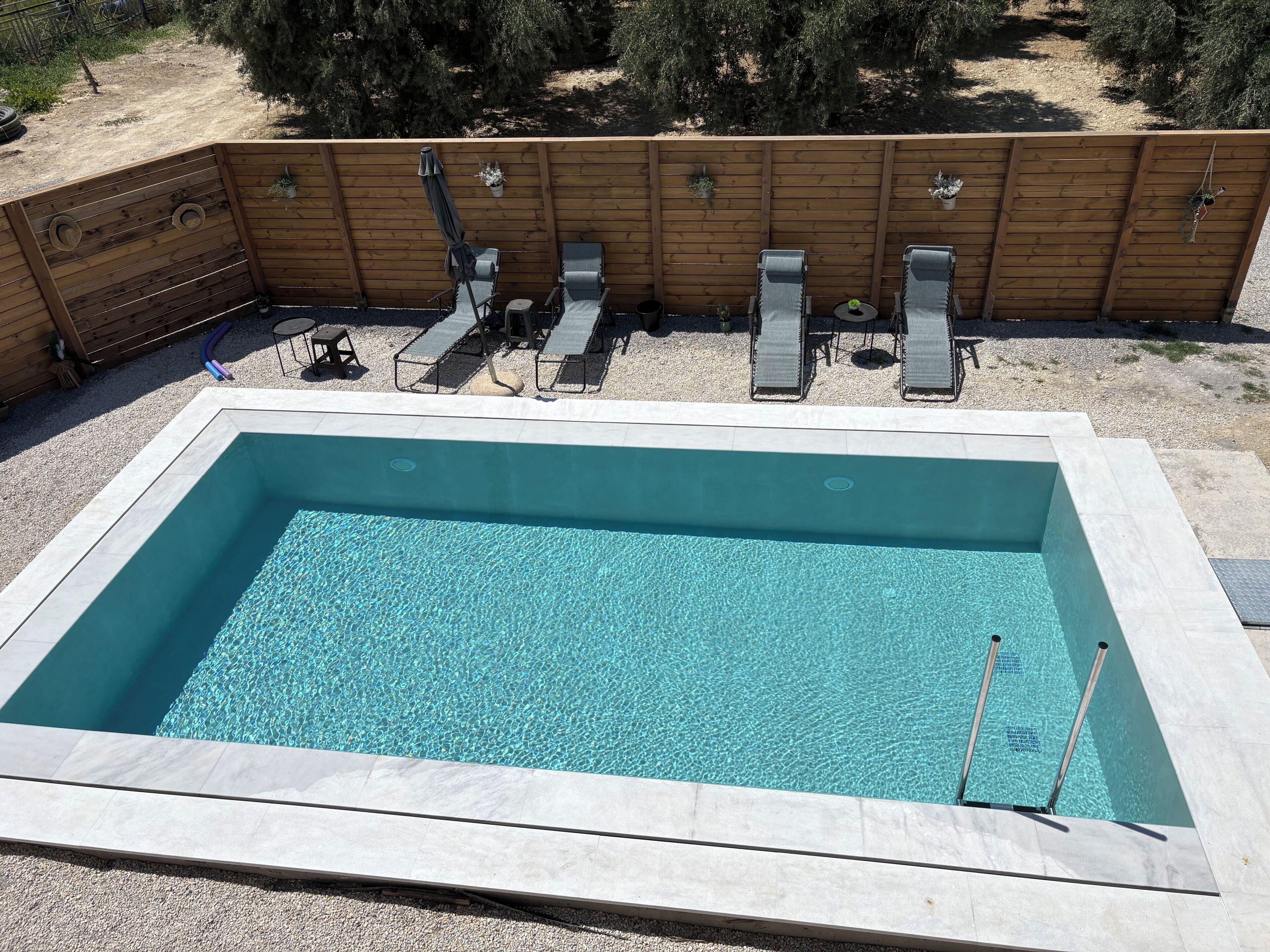 A rectangular swimming pool with a wooden deck surrounding it, equipped with lounge chairs and a hose for filling.