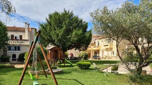 A residential area with a swing set, a small playhouse, and a dining area with outdoor seating. - Gîte Lucas 4 pers. piscine et clim à Sommières - Calm, nature & traditions ! (Sommières)
