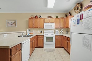 A kitchen with wooden cabinets, a white stove, a microwave, and a refrigerator.