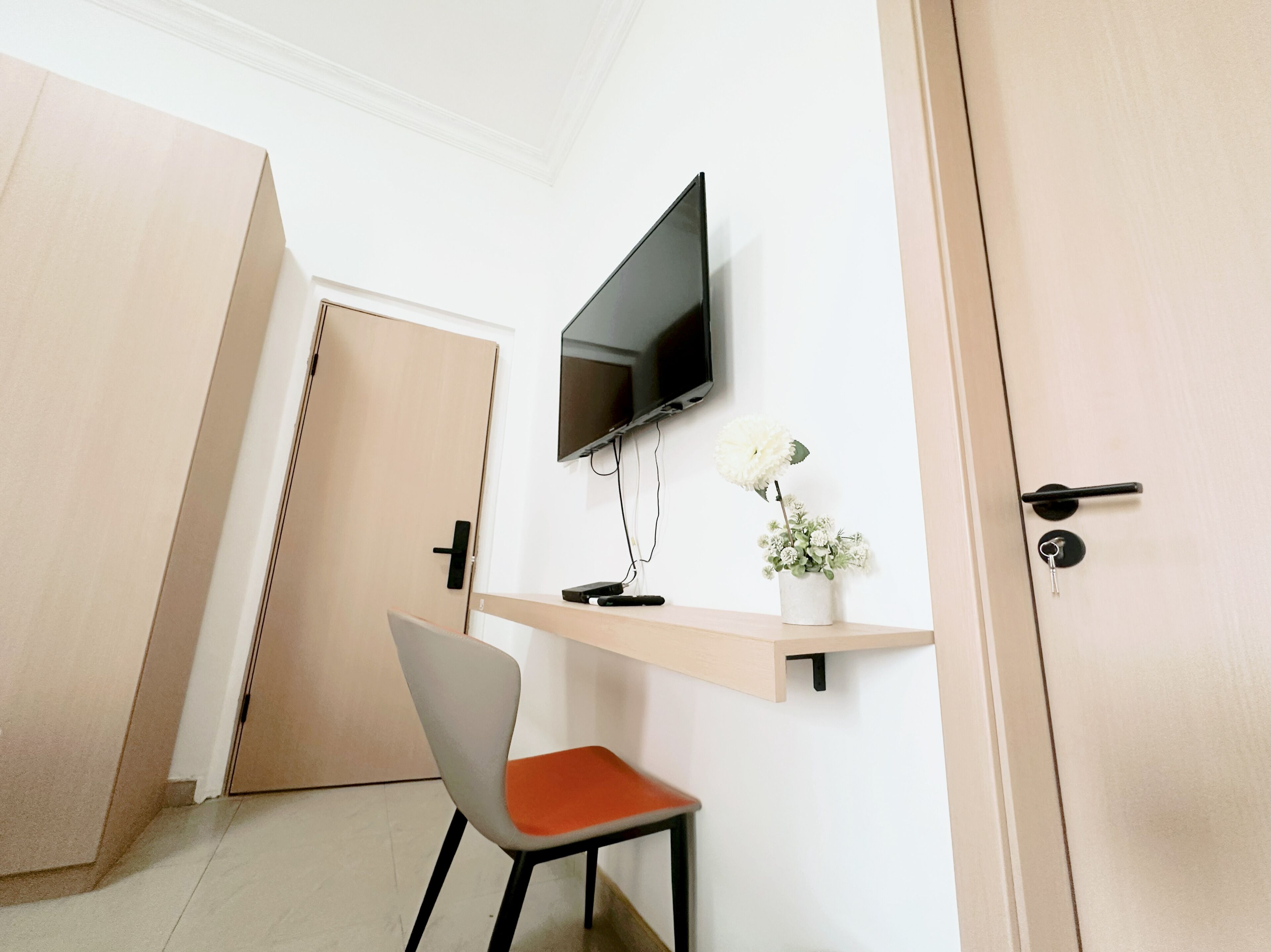 A hotel room with a TV mounted on the wall, a small table with a vase of flowers, and a chair.