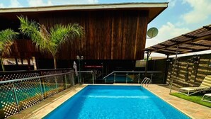 Una piscina rectangular con agua azul cristalina, rodeada por un solado de baldosas y una cerca de madera.