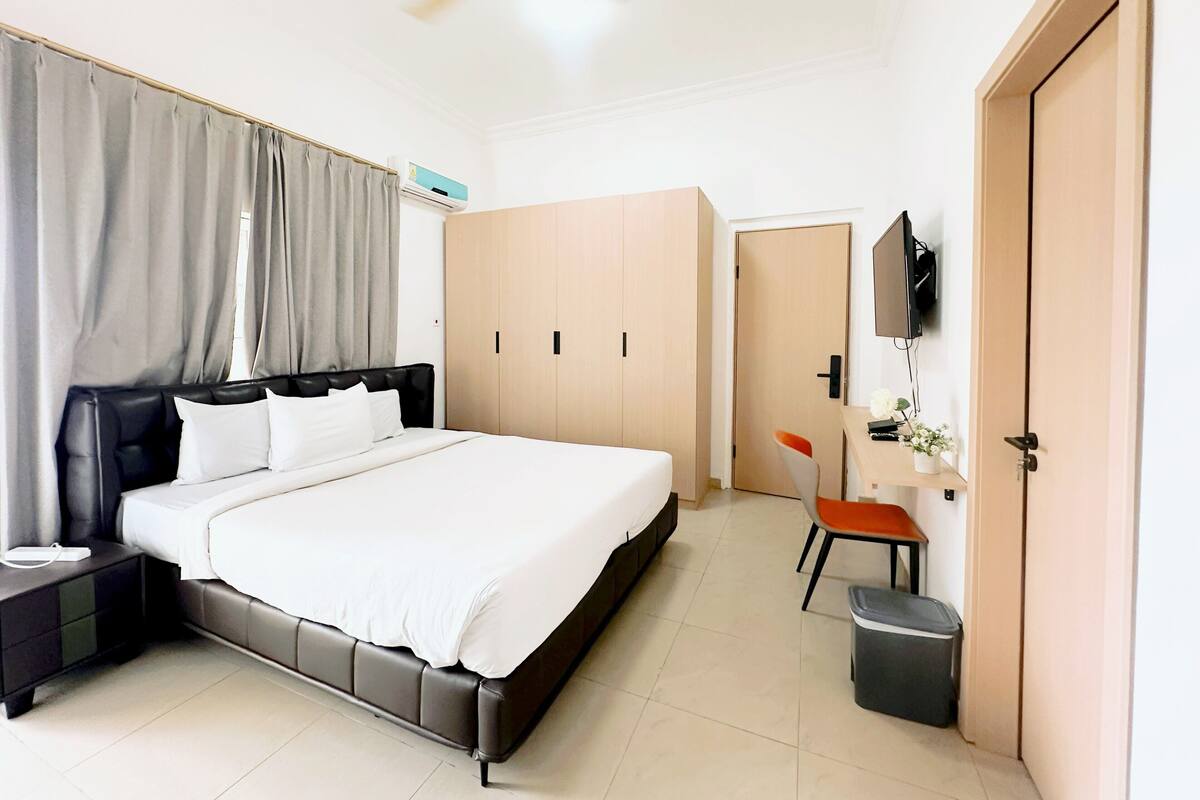 Un dormitorio moderno con cama, escritorio, silla, armario, televisor y ventilador de techo.