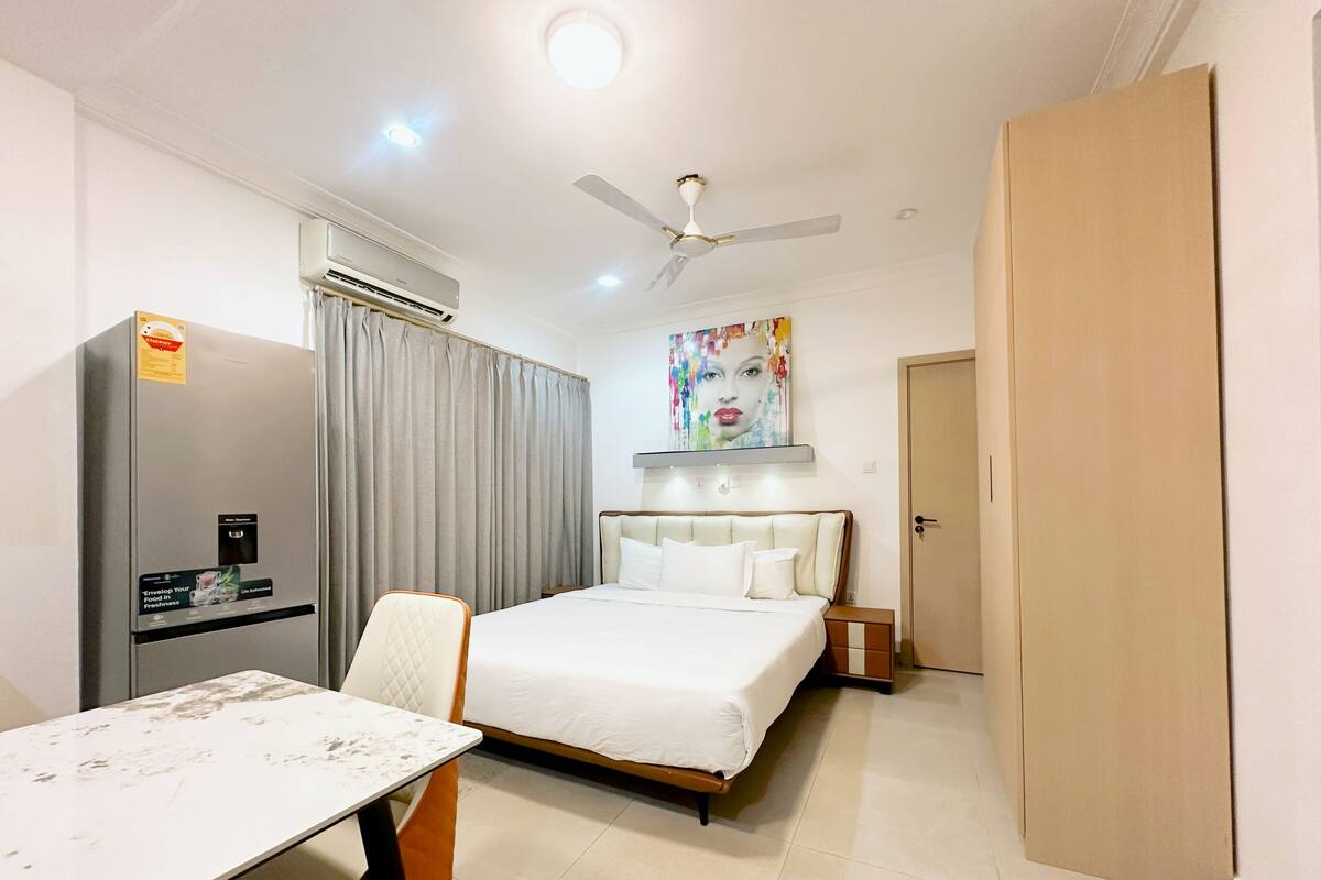 Habitación de hotel con cama, escritorio, silla, equipo de aire acondicionado, ventilador de techo y puerta.