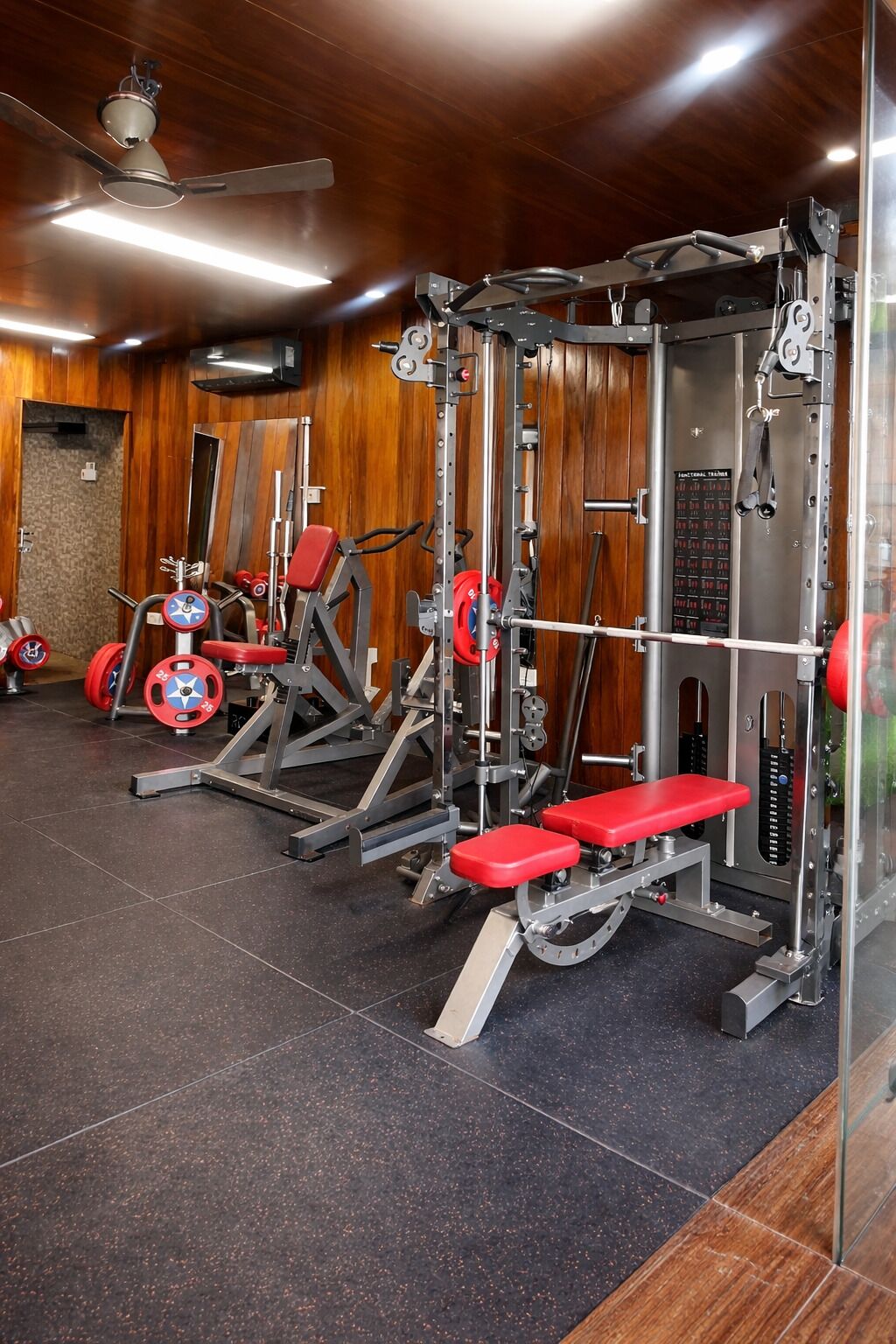A gym with weightlifting equipment, a ceiling fan, and wooden walls.