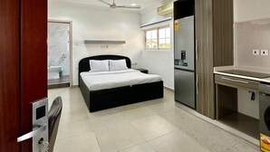 A compact bedroom with a bed, a desk, and a kitchenette. - Golden Crystal Hotel (Accra)