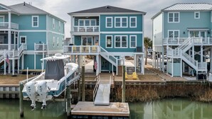A waterfront property with multiple levels, a dock with boats, and a small deck area. - Dancing Pelican-New 5-bedroom 3.5 baths, canal house w/elevator, 3min to beach (Holden Beach)