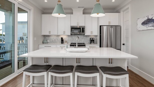 A modern kitchen with white cabinets, a central island, bar stools, and pendant lighting. - Dancing Pelican-New 5-bedroom 3.5 baths, canal house w/elevator, 3min to beach (Holden Beach)