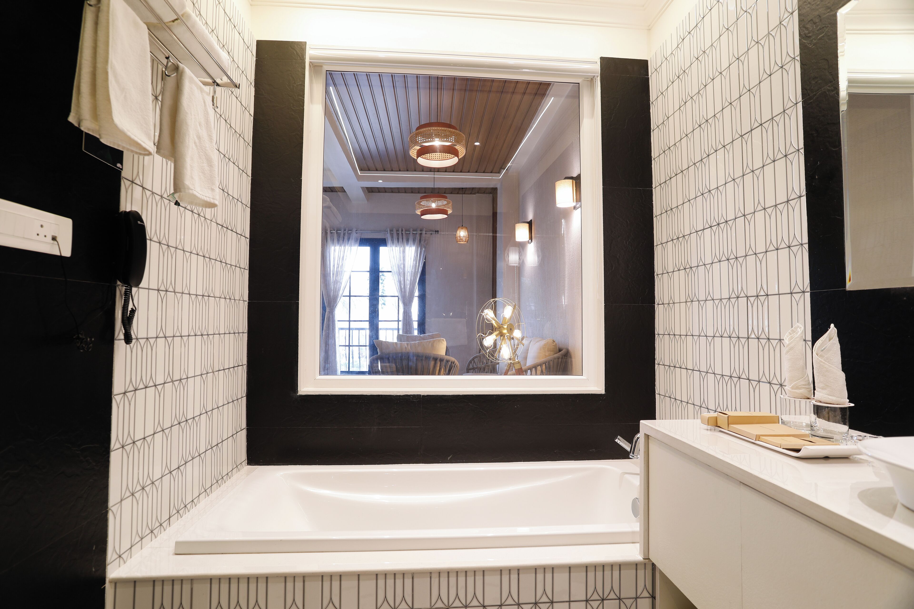 Un baño moderno con una bañera grande, una ventana que ofrece vistas a una sala de estar y una pared con azulejos de diseño geométrico.