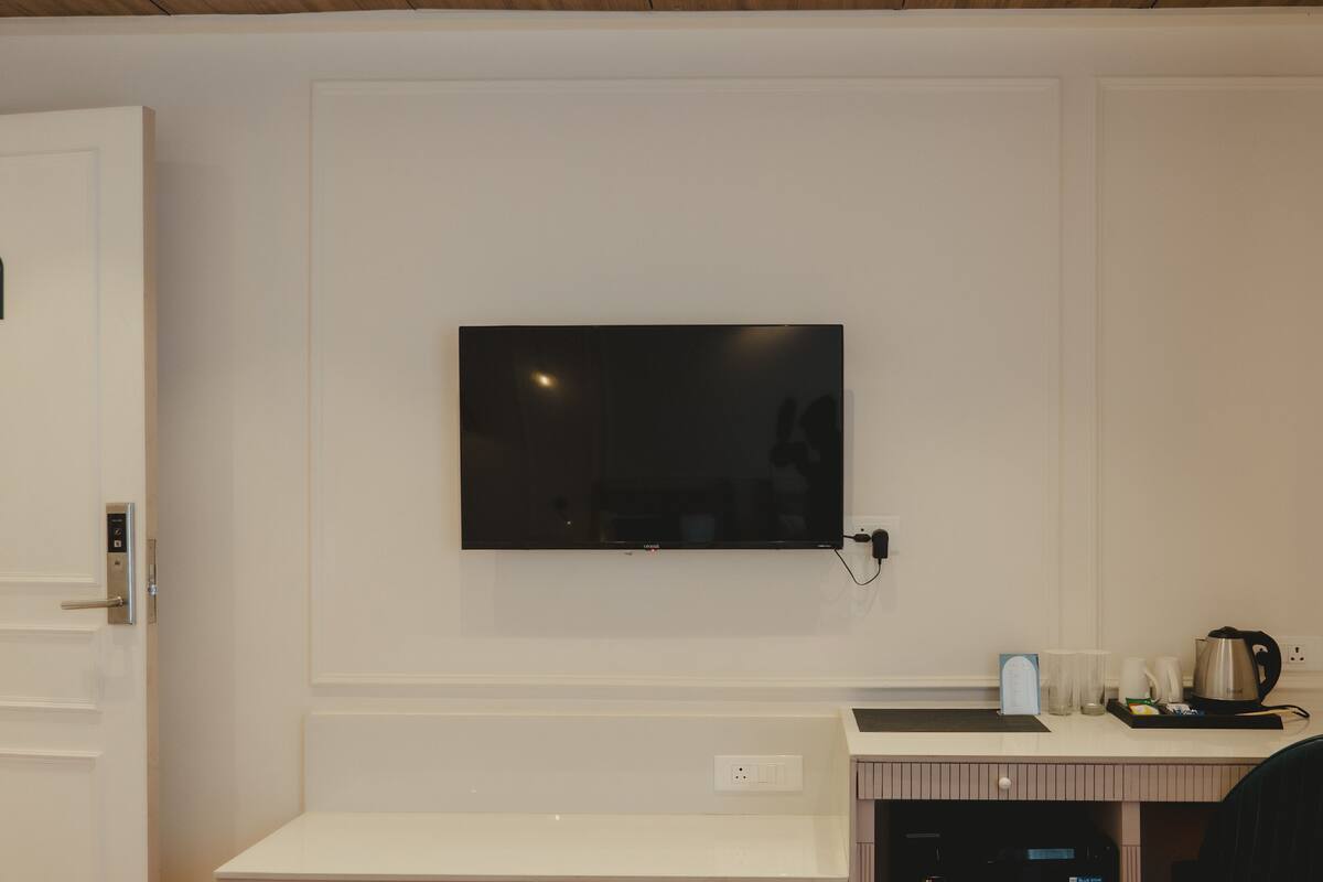 A hotel room with a flat-screen TV mounted on the wall, a desk with a laptop, a coffee maker, and a chair.