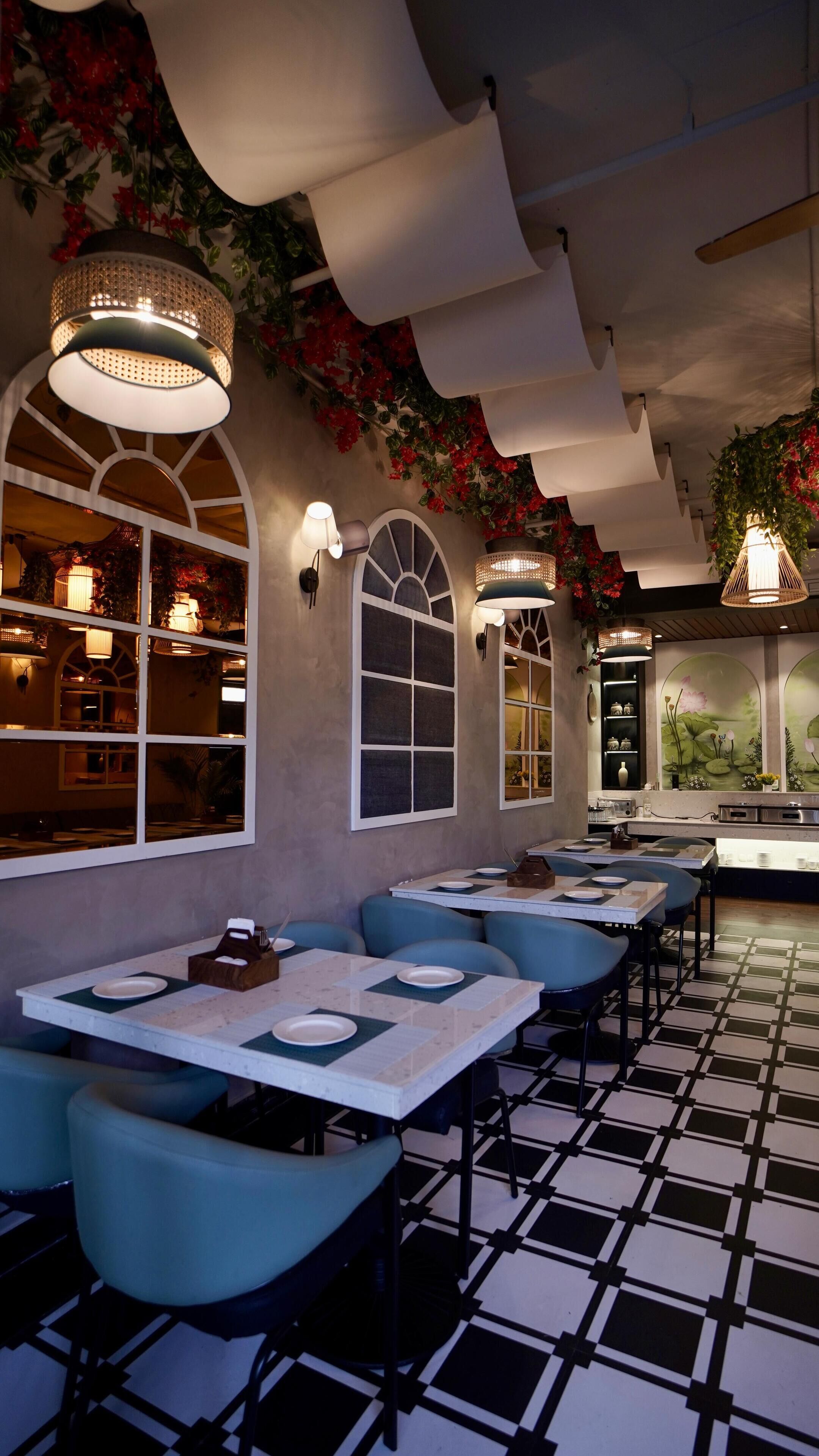 A restaurant interior with high tables and blue cushioned booths, decorative ceiling panels, and wall-mounted lighting fixtures.