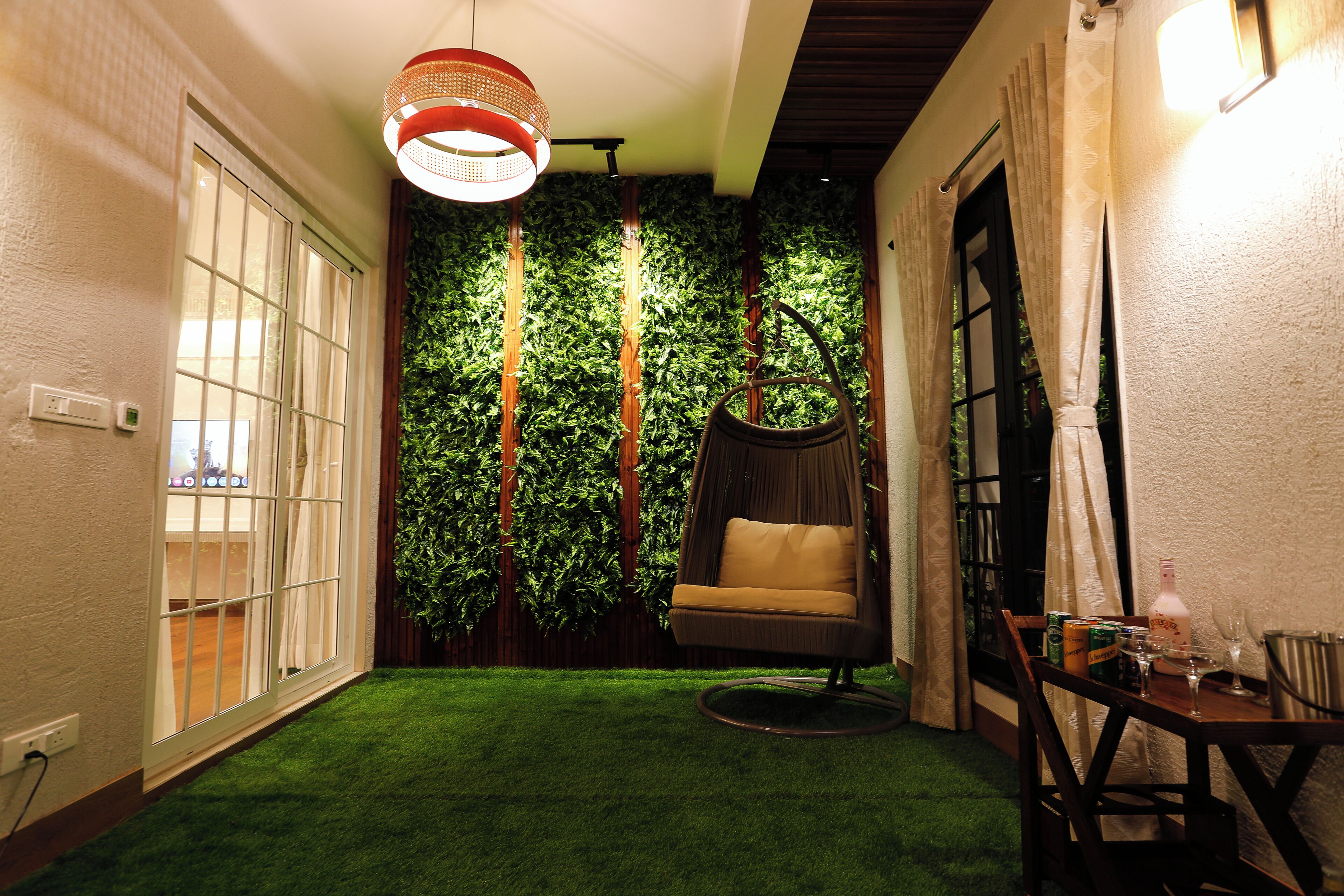 A cozy indoor space with a green artificial grass floor, a hanging chair, a dining table with chairs, and a wall with vertical greenery.