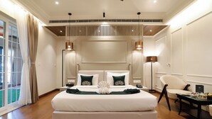 A spacious bedroom with a large bed, a sitting area with a chair, and a view of the outdoors through a sliding door. - Narayan kothi (Varanasi)