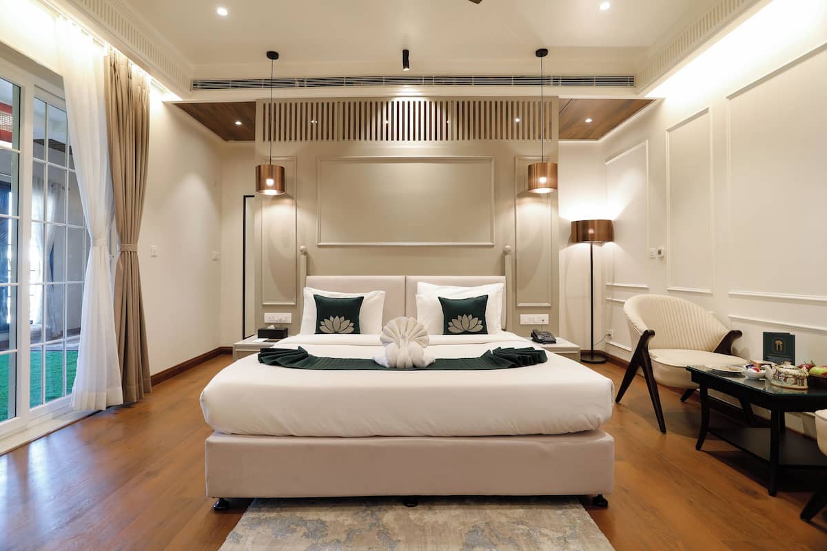 A spacious bedroom with a large bed, a sitting area with a chair, and a view of the outdoors through a sliding door.
