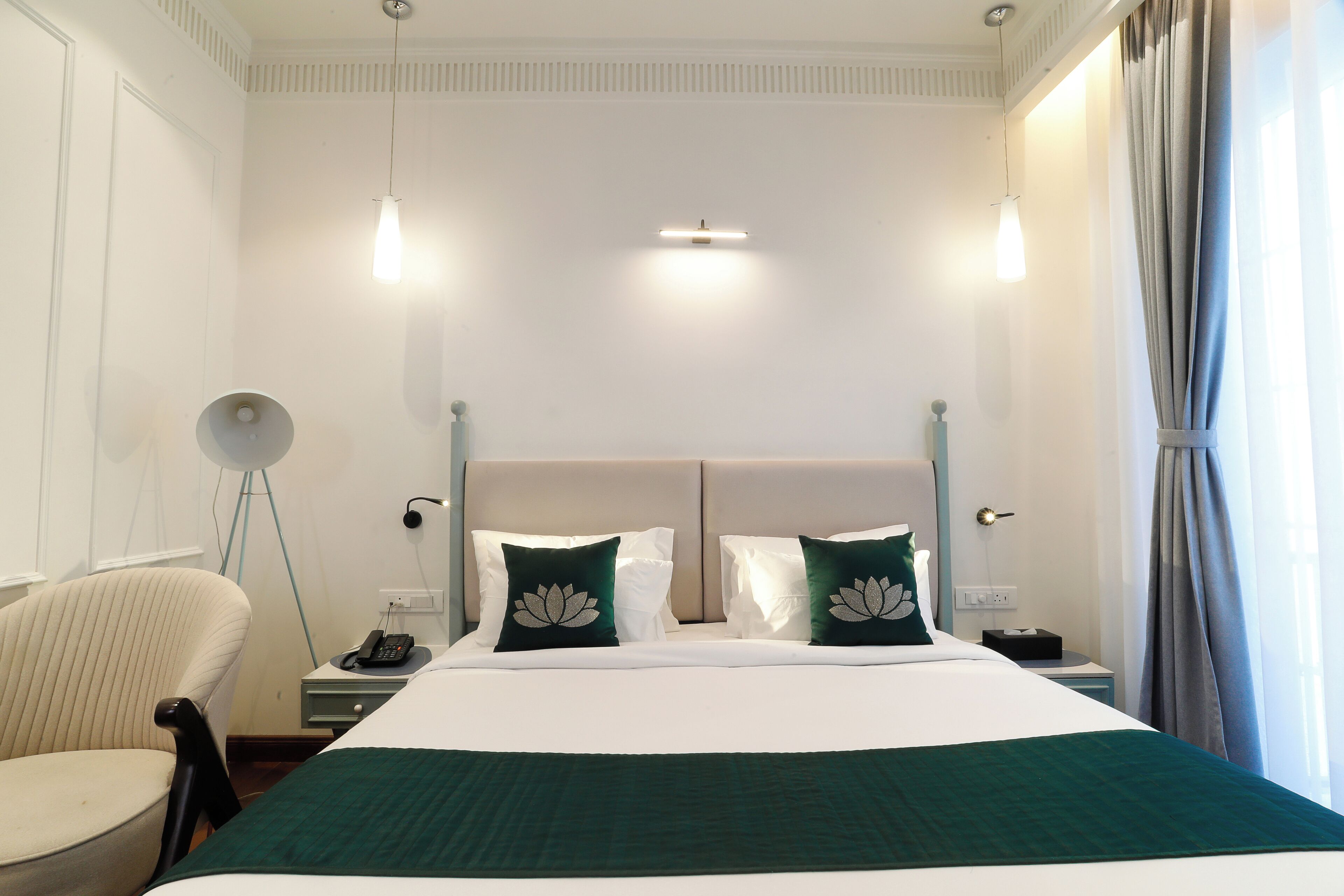 A hotel room with a bed, a chair, a bedside table with a lamp, and a window with curtains.