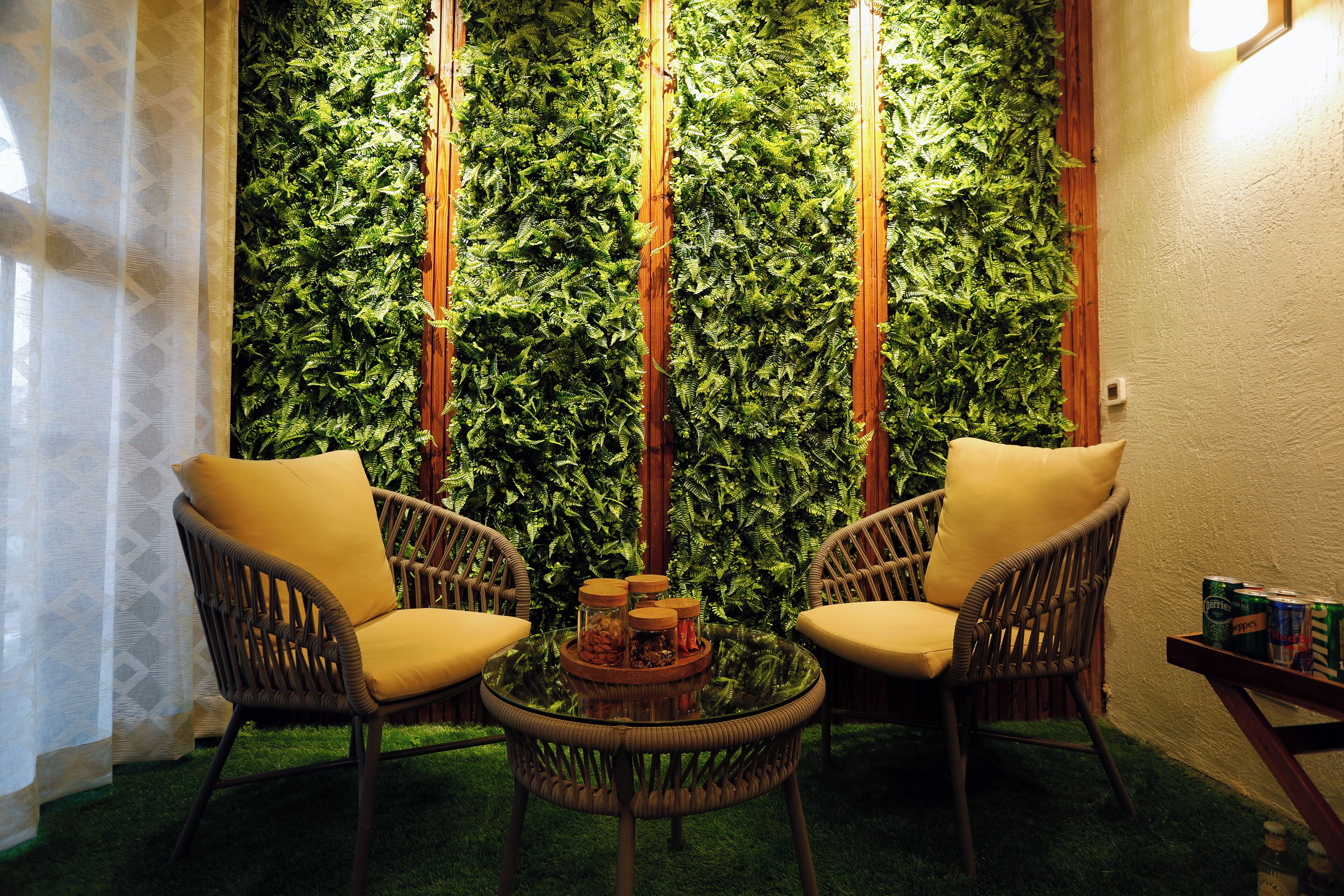A room with two wicker chairs, a small round table with a tray of snacks, and a wall covered in green foliage.