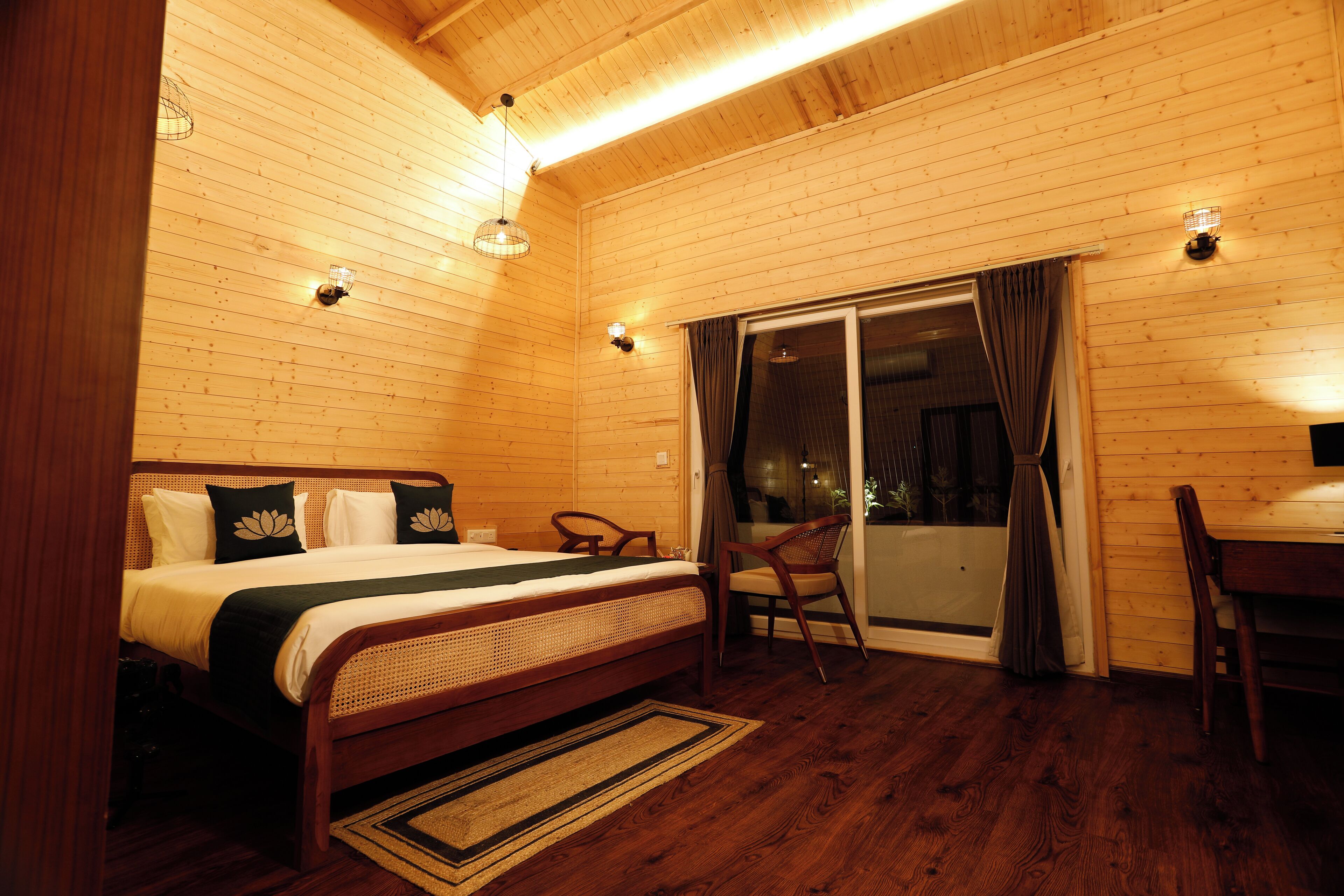 A wooden cabin bedroom with a bed, chairs, a table, and a sliding glass door.