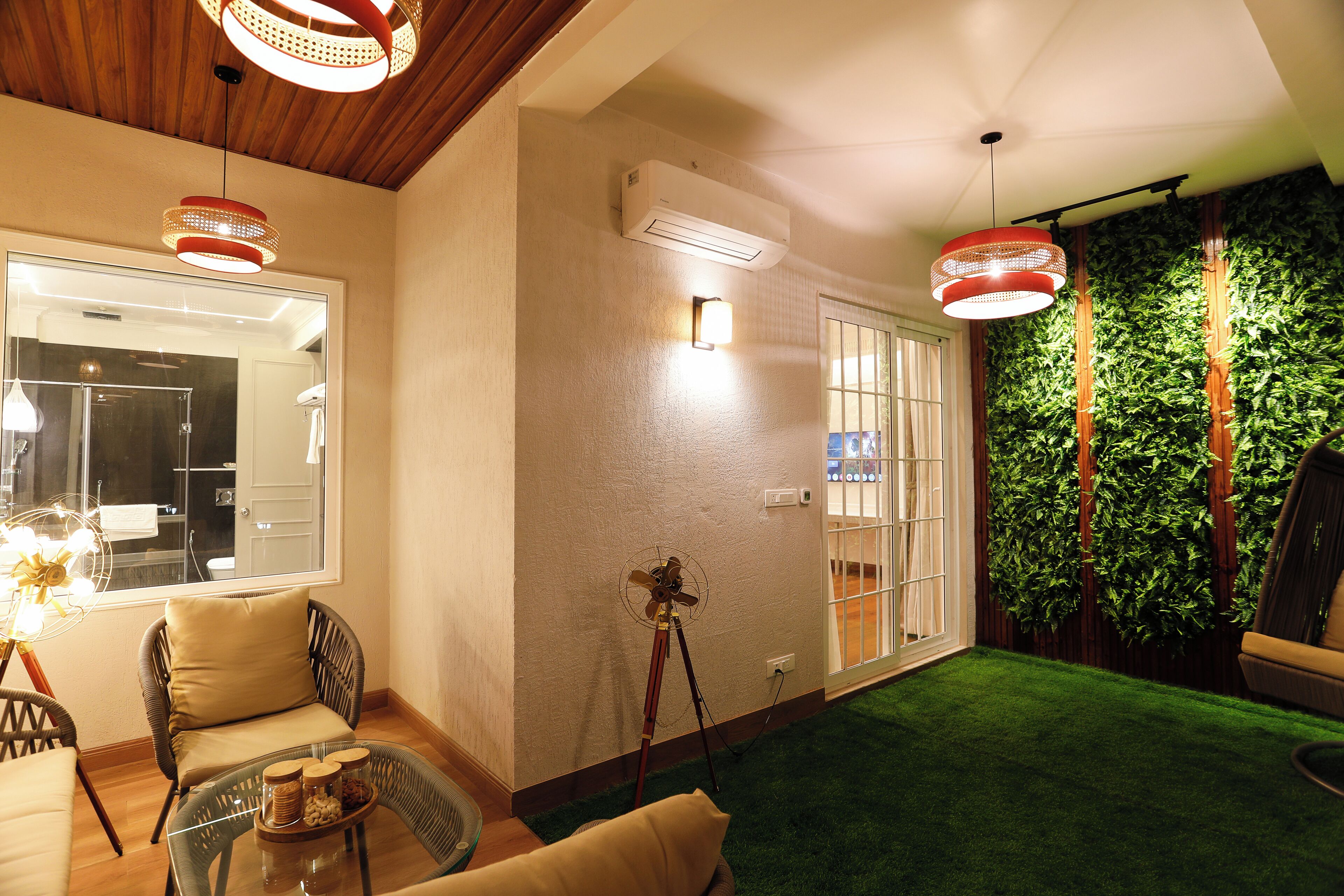 A room with a wooden ceiling, a glass table with a tray of snacks, a wicker chair, a floor lamp, and a wall-mounted fan.