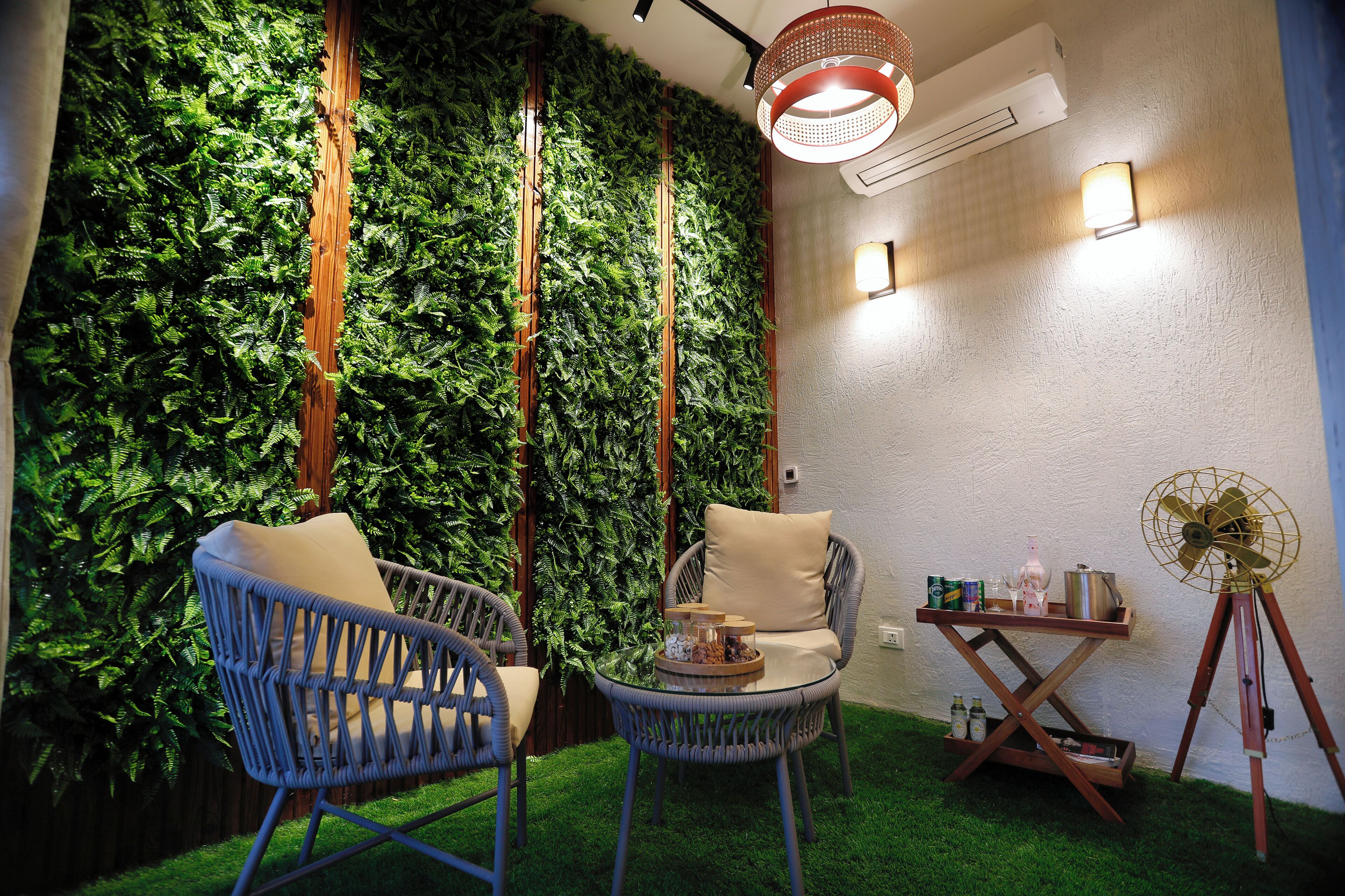 A cozy indoor seating area with wicker chairs, a small round table, and a wall adorned with green foliage.