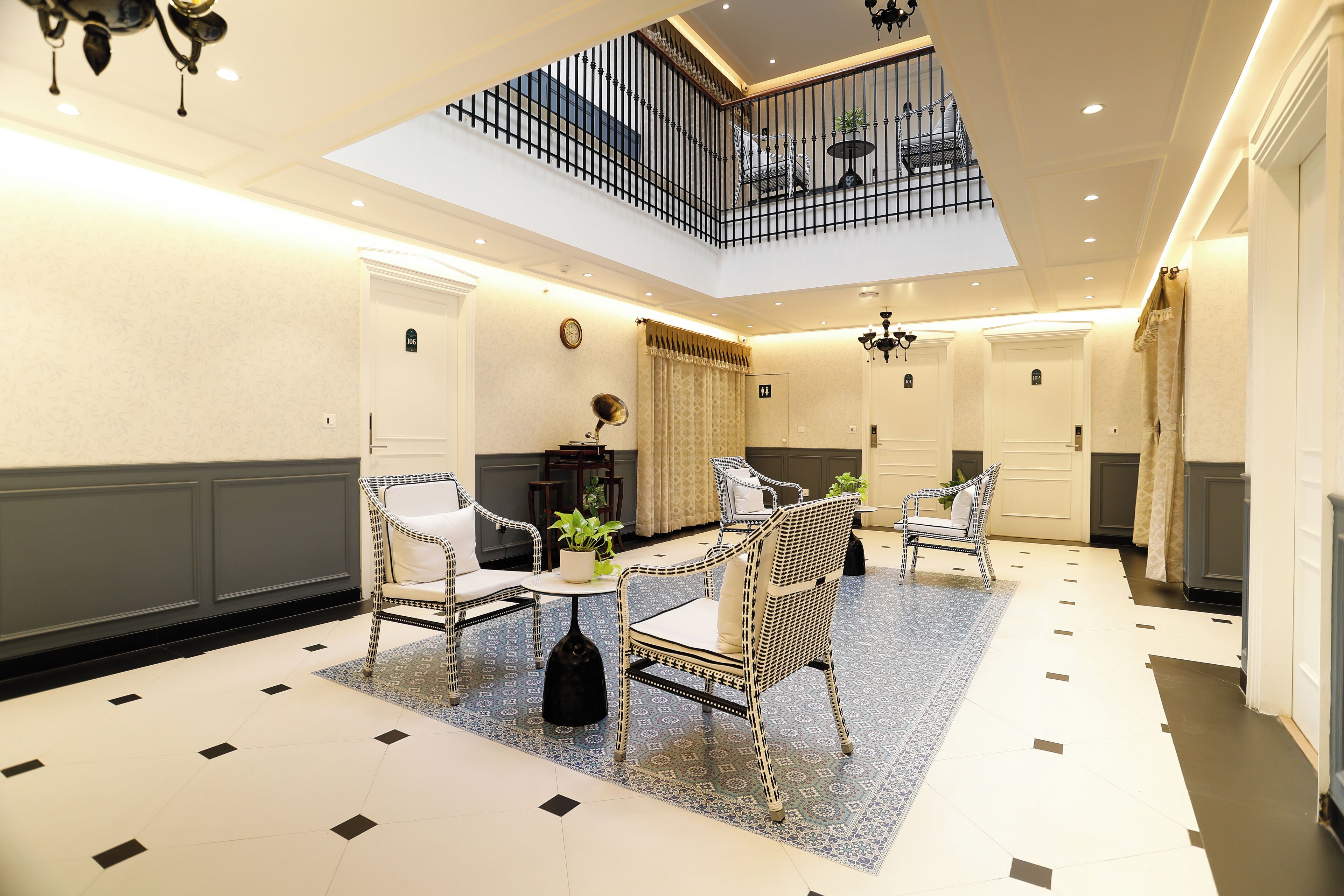 Un'ampia hall con soffitto alto, un'area salotto centrale con sedie e un tavolo, e una scala che conduce a un piano superiore.