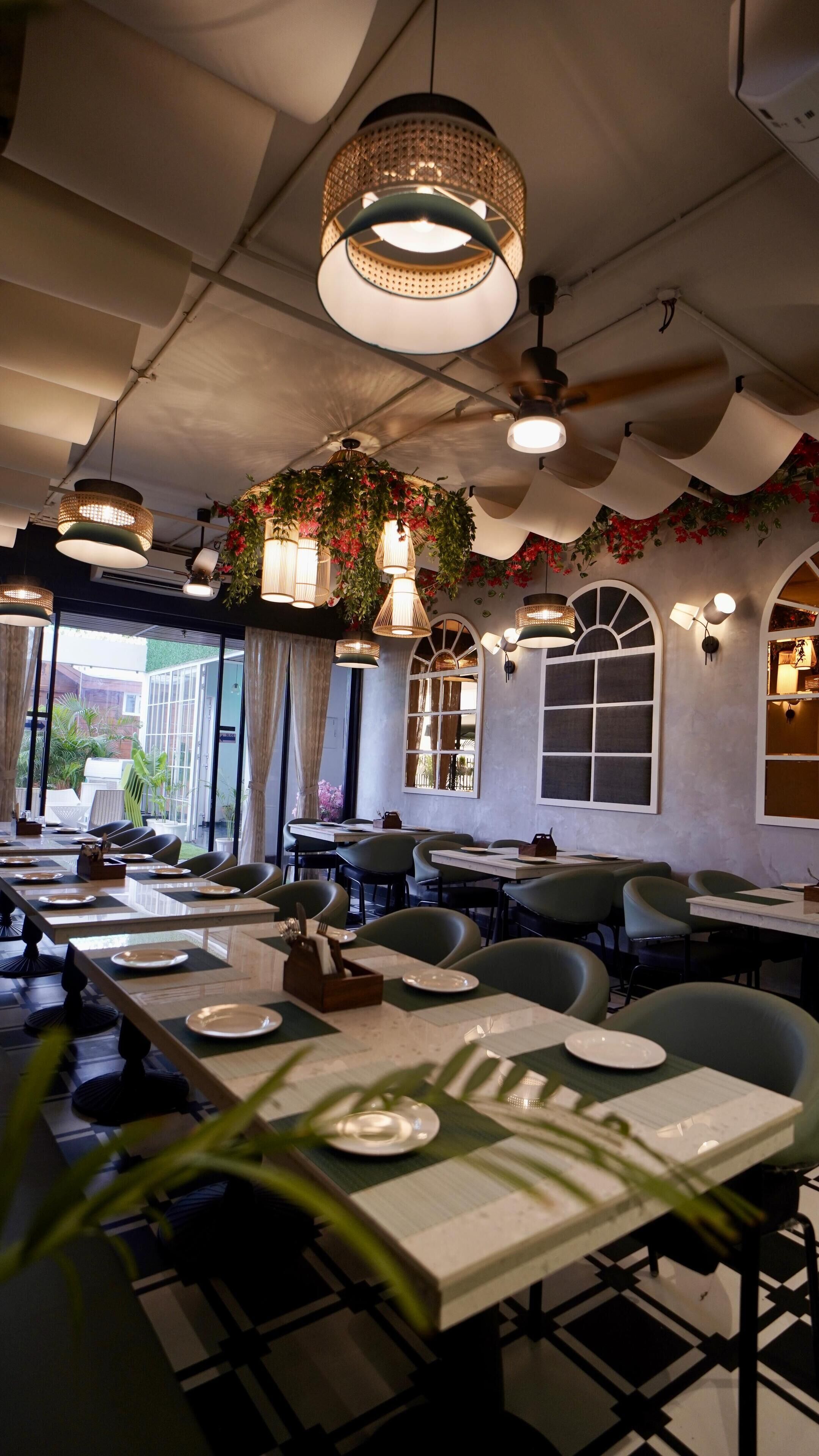 Un restaurante con varias mesas, plantas colgantes e iluminación colgante.