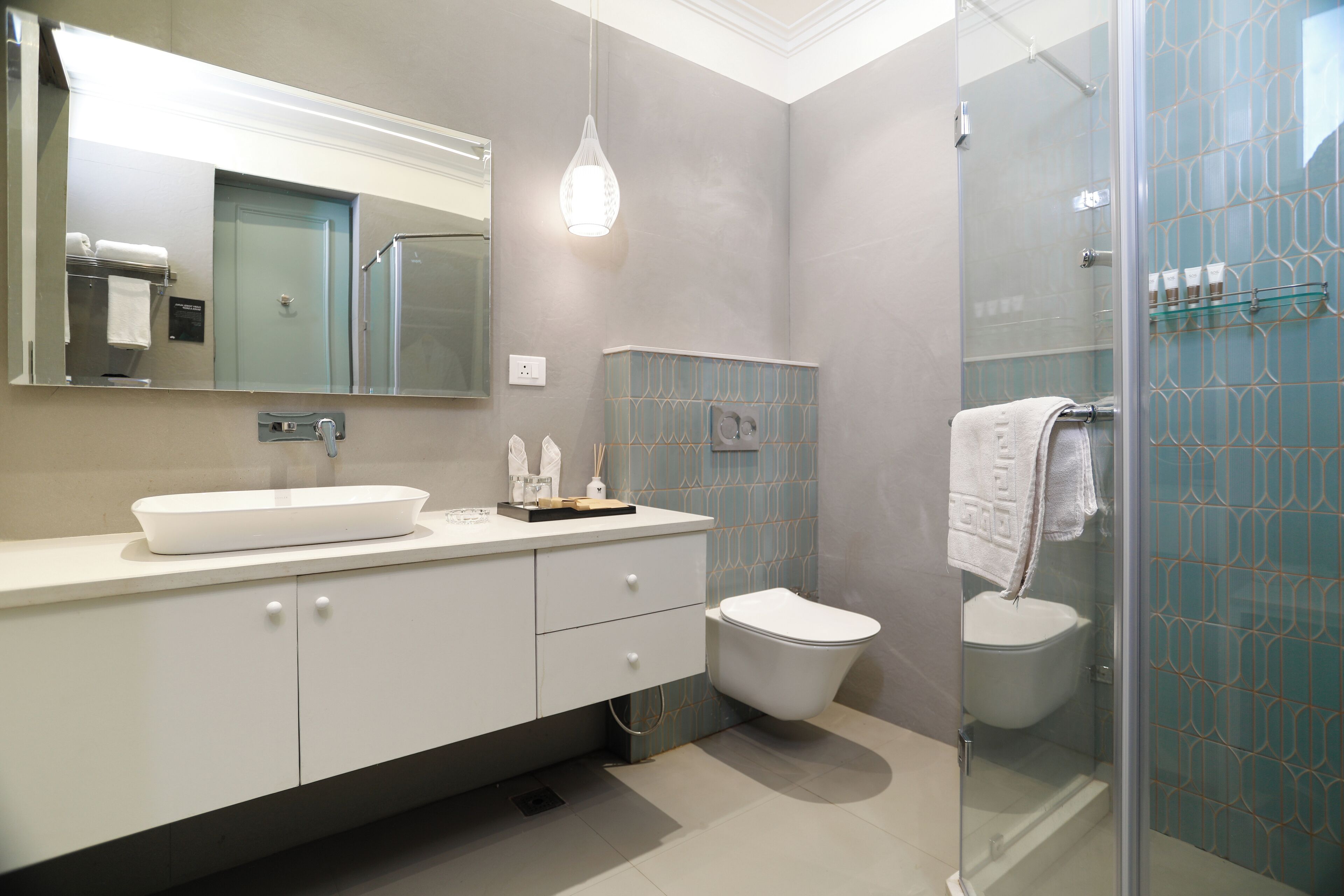 A modern bathroom with a large mirror, a white sink, a toilet, and a glass shower enclosure.