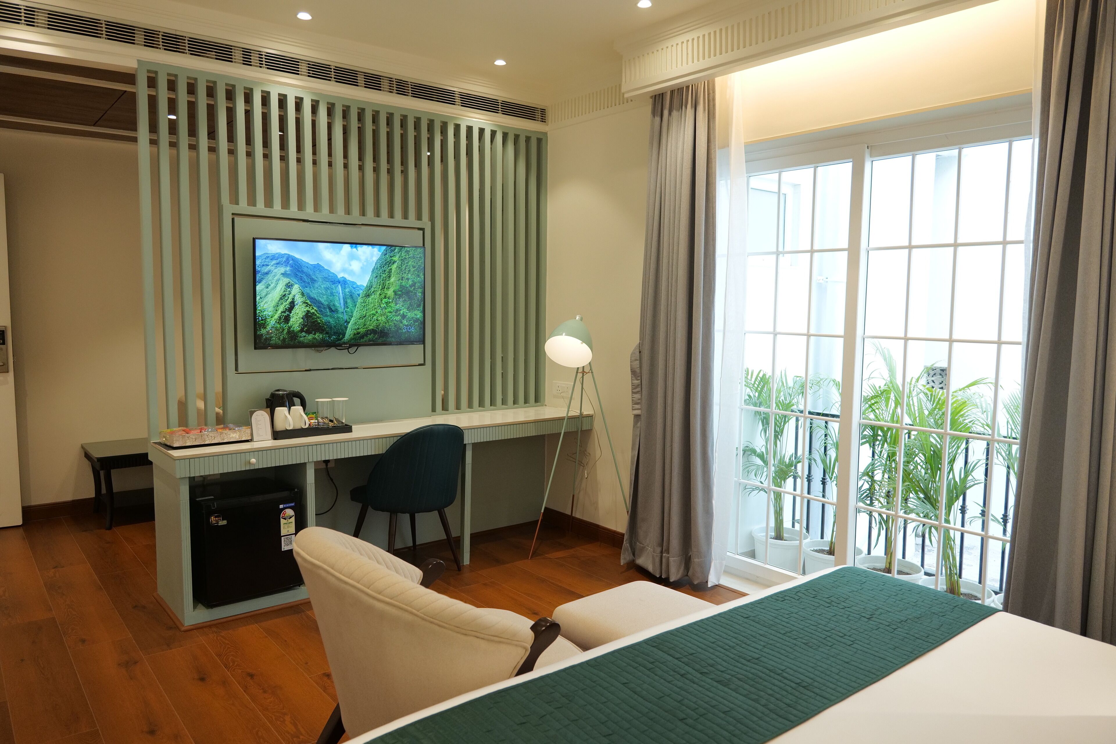 Une chambre d’hôtel avec un lit, un bureau équipé d’un ordinateur, une chaise, une télévision et une fenêtre avec des rideaux.